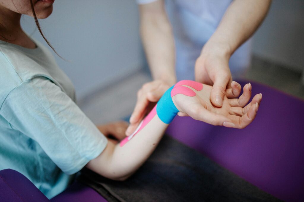 Unterarm einer Person mit elastischem Tape an Handgelenk und Unterarm, gehalten von einer anderen Person