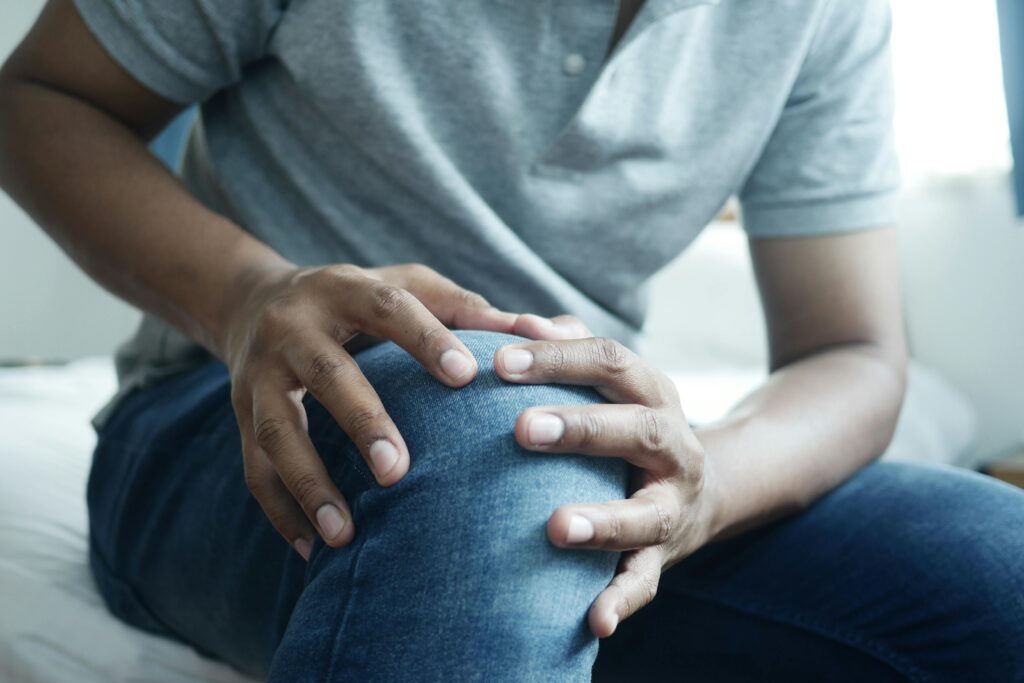 Ausschnitt einer Person, die ihr Knie mit beiden Händen umfas